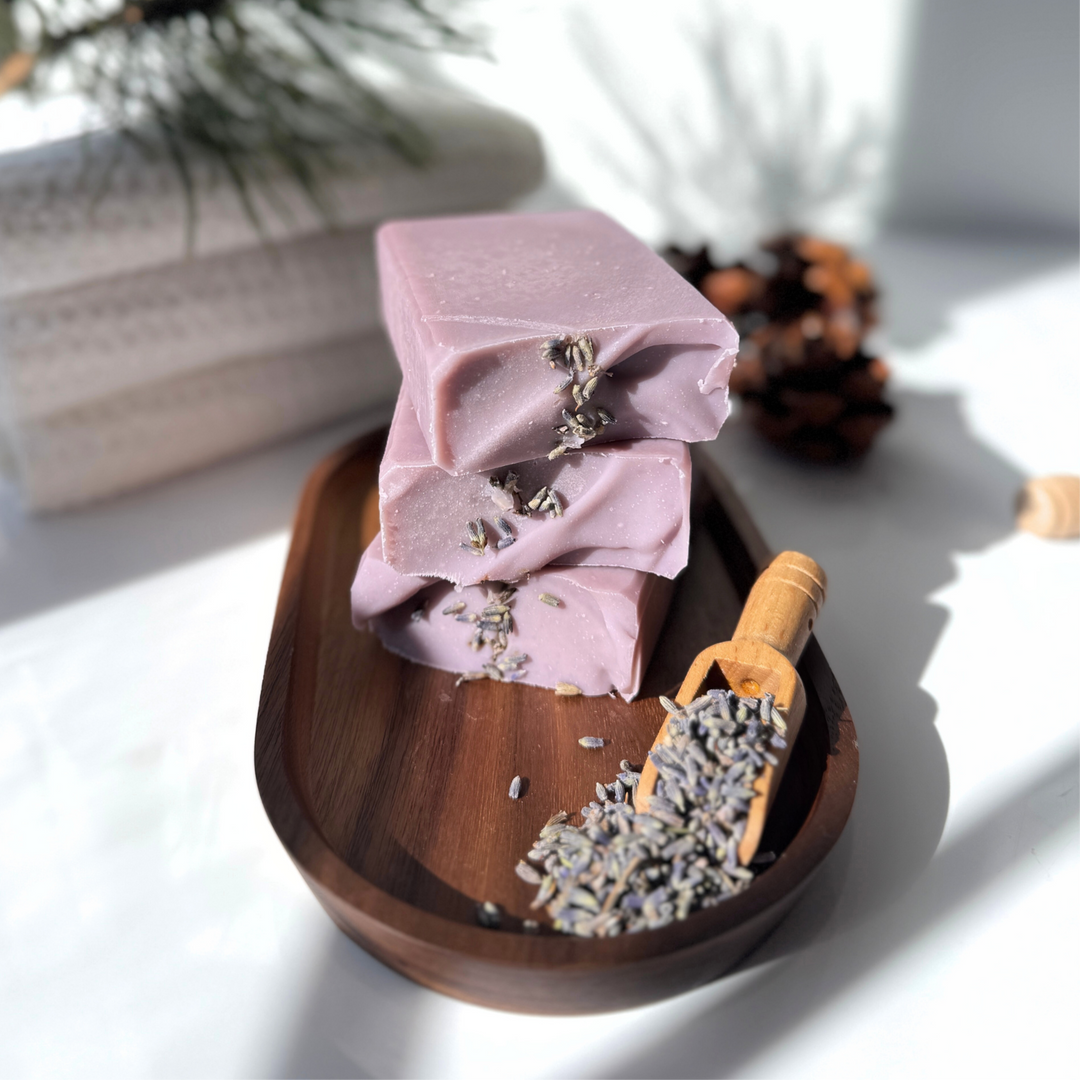 Purple soap bars with lavender on a wooden tray on a light surface.