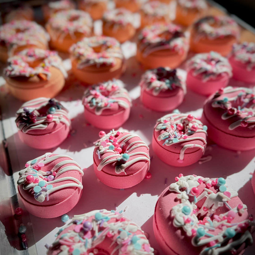 Decorative pink donut-shaped bath bombs with colorful sprinkles on a pink surface.