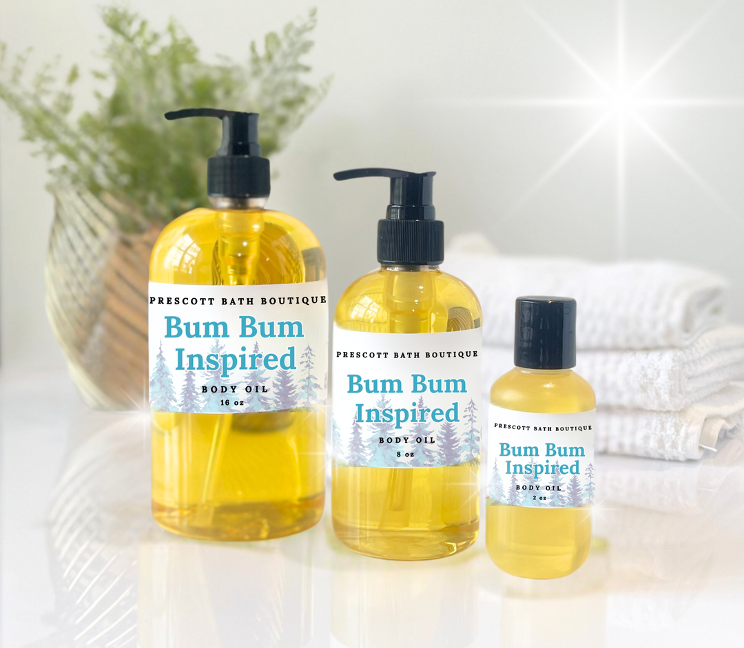 Three bottles of 'Bum Bum Inspired' body oil from Prescott Bath Boutique on a white surface with a blurred background.