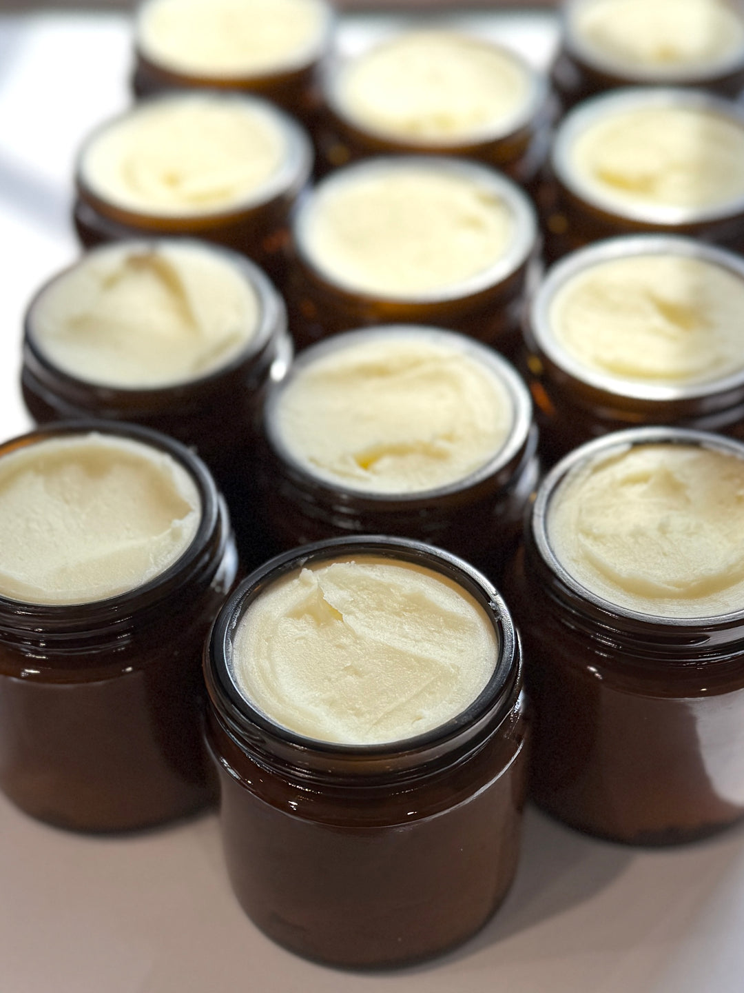 Multiple small brown jars filled with a white cream-like substance on a light background.