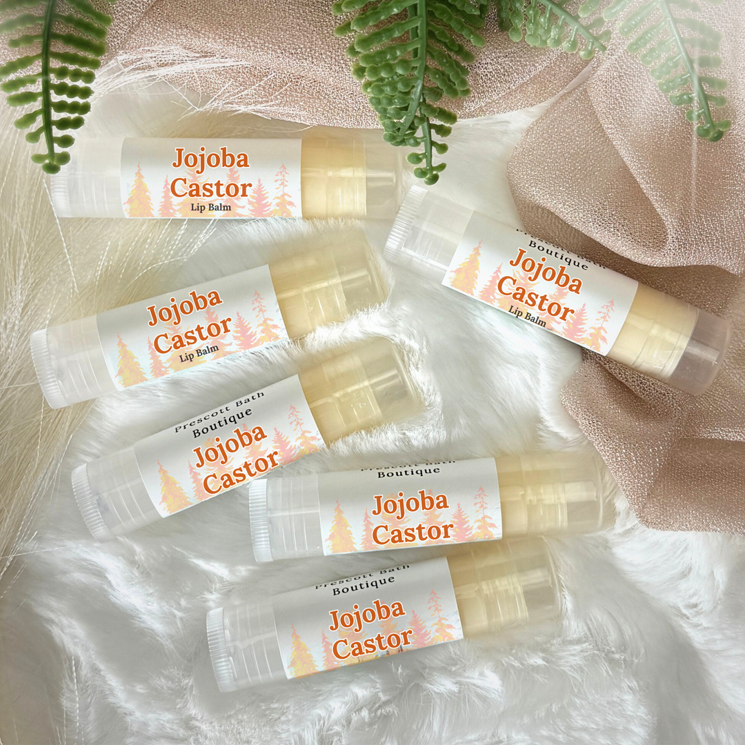 Multiple Jojoba Castor lip balms on a textured surface with green leaves.